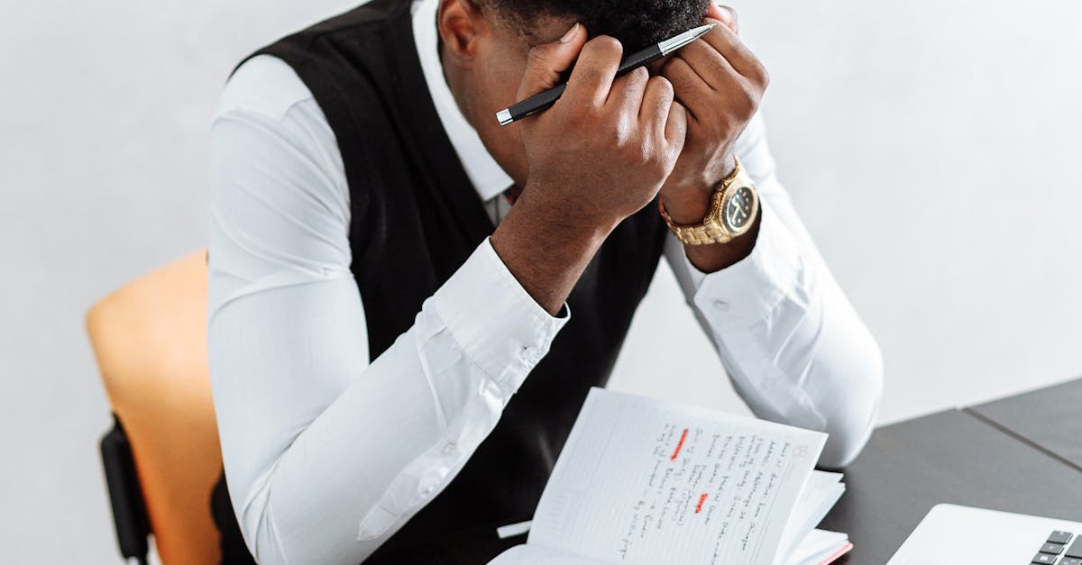 Man in White Dress Shirt Sitting on Chair in Front of Table With Macbook Pro