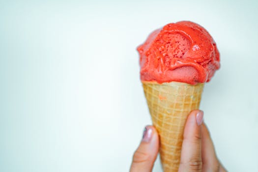 Close-up of a strawberry ice cream cone held by hand, showcasing vibrant color and tempting texture.