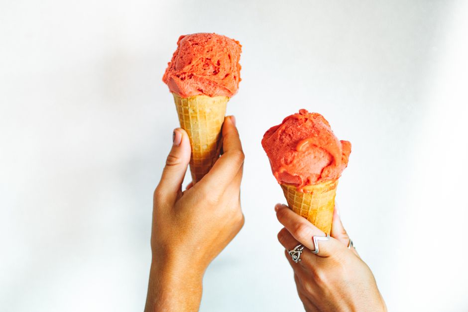 Close-up of two hands holding strawberry ice cream cones against a white background.