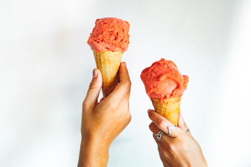 Free Close-up of two hands holding strawberry ice cream cones against a white background. Stock Photo