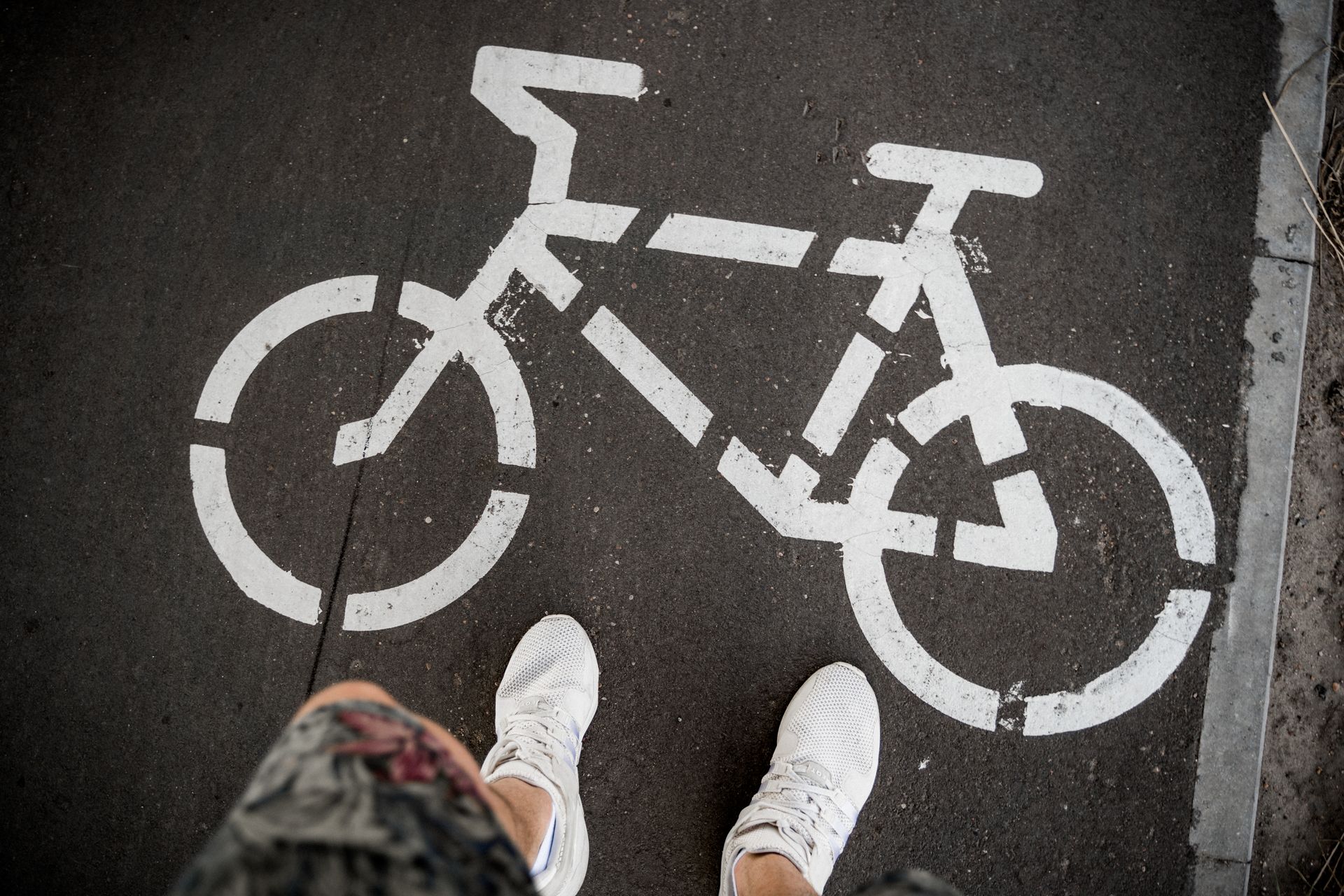 White sneakers standing on a bicycle lane symbol painted on the pavement.