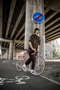 一名年轻人骑着自行车，站在城市里禁止自行车标志附近的桥下