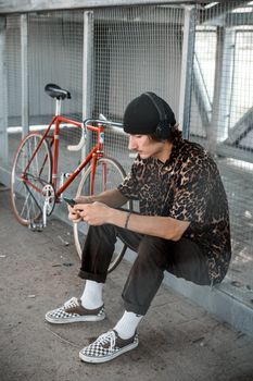 一名年轻人戴着耳机，坐在自行车旁打电话