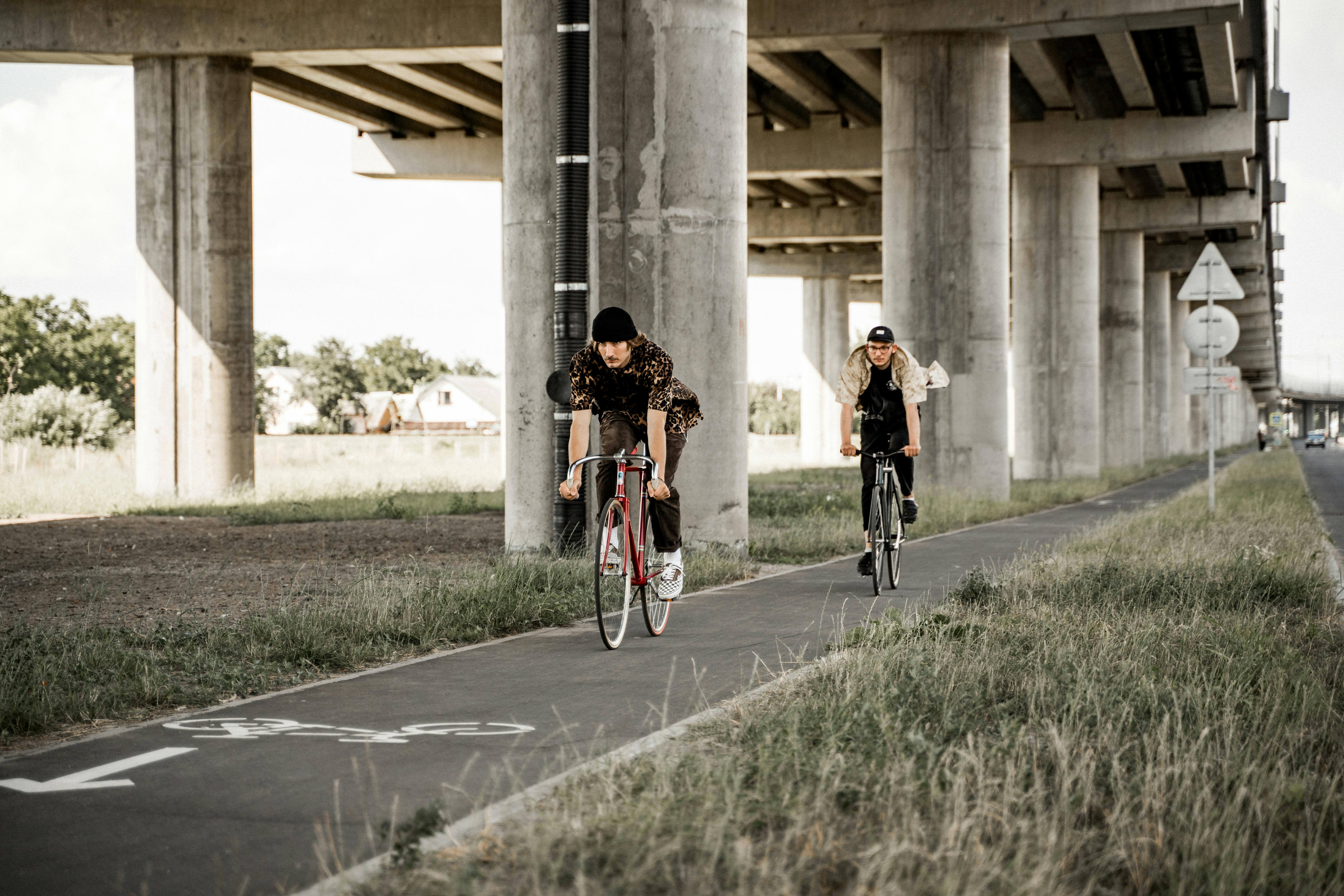 Two young men enjoy a casual bike ride on a designated bike lane under an urban bridge.
