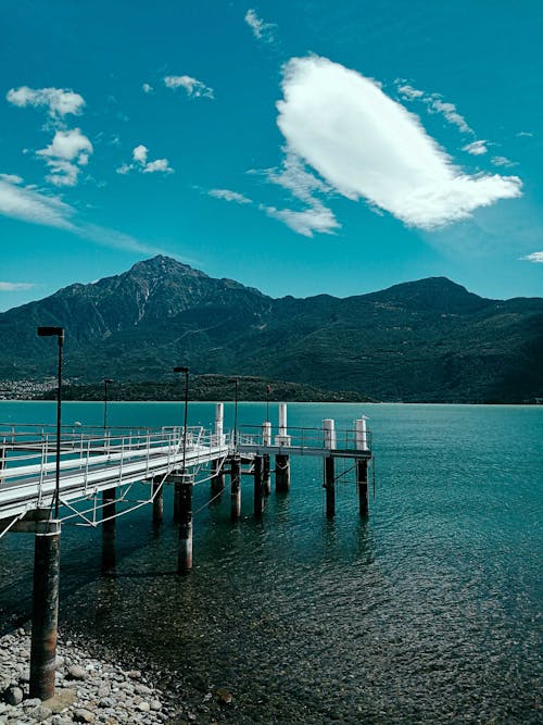 Free Scenery view of empty wooden walkway on shore of peaceful lake surrounded by rocky mountains covered with forest Stock Photo