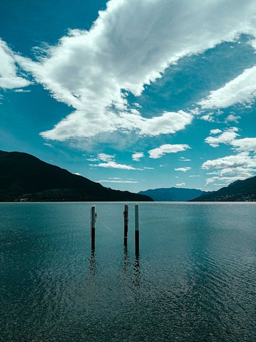 Picturesque scenery of tranquil lake with poles rippling at bottom of rough rocky mountains beneath clear blue sky