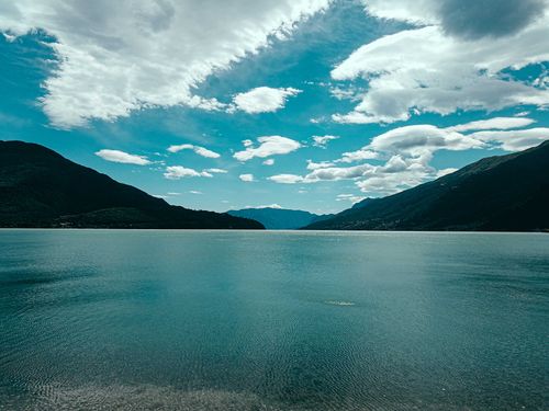 Free Scenic landscape of rough grassy mountains surrounding tranquil rippling lagoon with blue seawater beneath bright blue sky Stock Photo