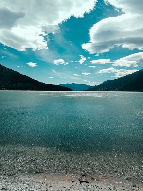 Free Scenic view of azure vast lake washing shore with rocky mountains beneath bright blue sky Stock Photo