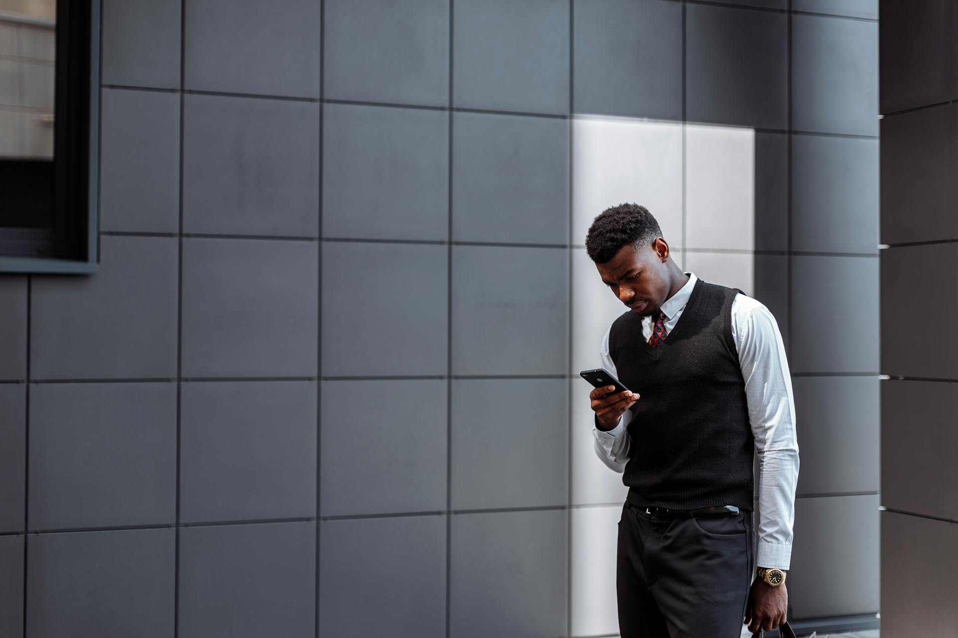 A modern business professional in formal attire using a smartphone outside an office building.