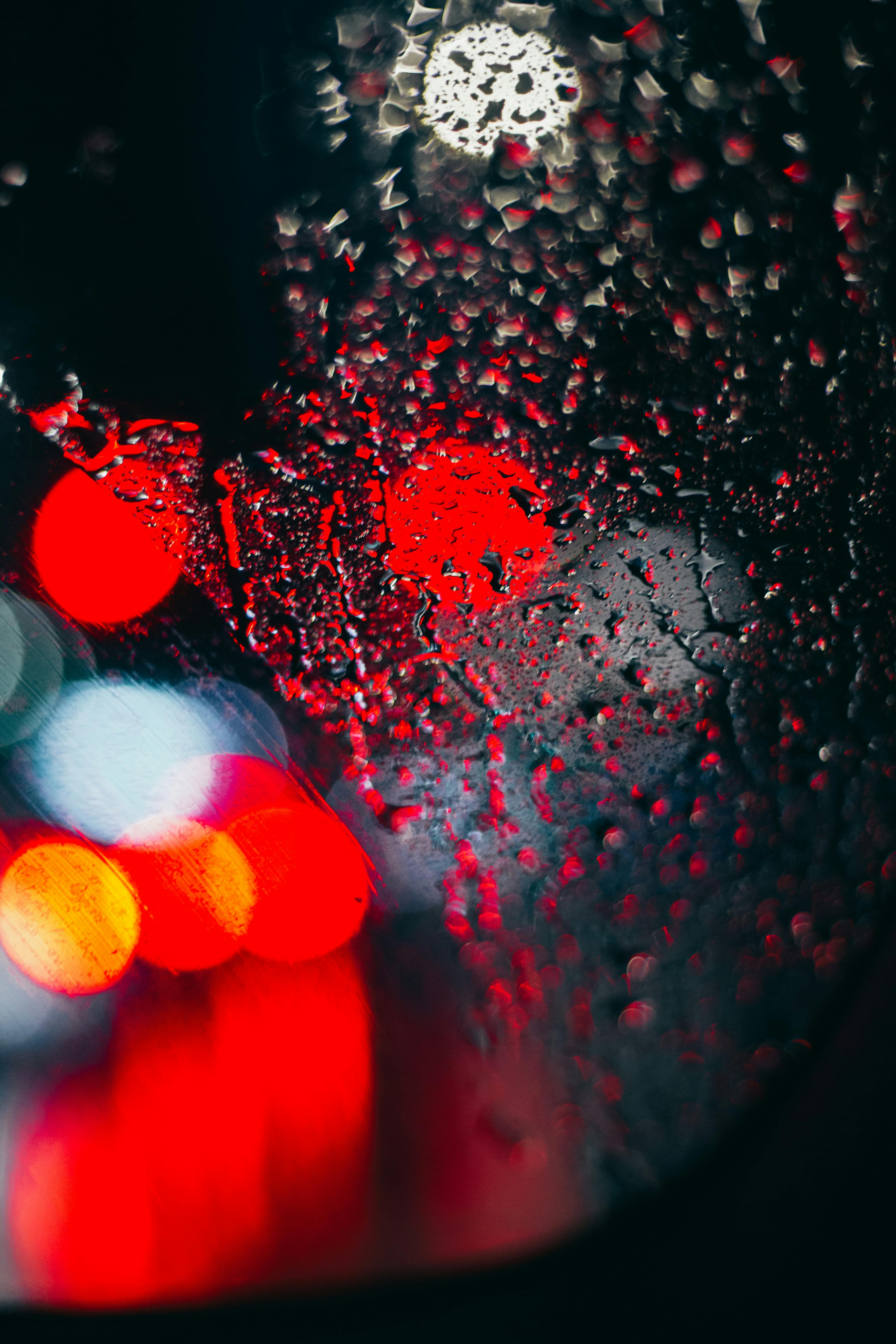Wet glass with raindrops and view of glowing red and white colored lights at night