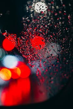 Artistic bokeh of raindrops on a car window with red and white lights at night.