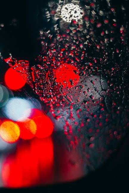 Wet glass with raindrops and view of glowing red and white colored lights at night