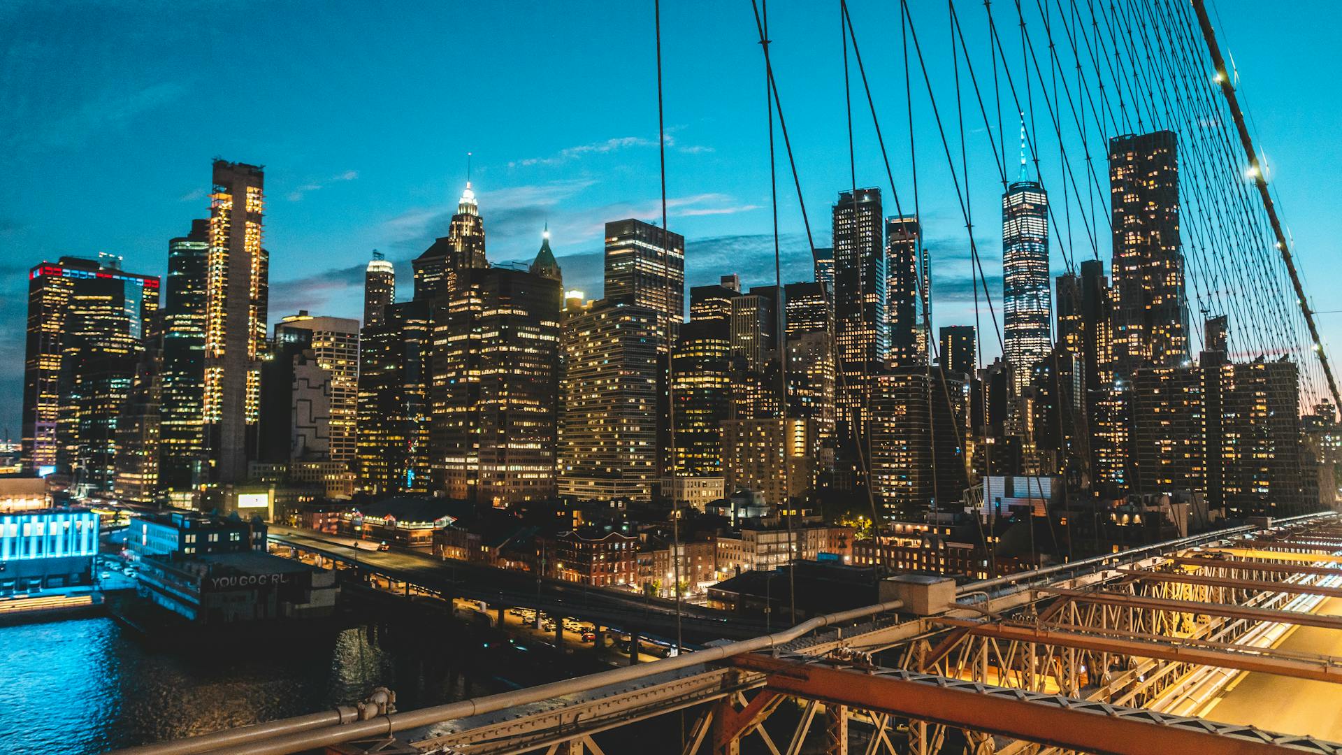 Panoramic view of New York City skyline at twilight from Brooklyn Bridge, showcasing modern skyscrapers.