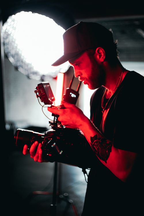 Free A cinematic shot of a male filmmaker adjusting camera equipment in a dim studio light. Stock Photo