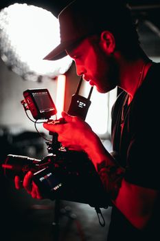 A bearded man adjusts digital movie camera equipment in a dimly lit setting, focusing on video recording technology.