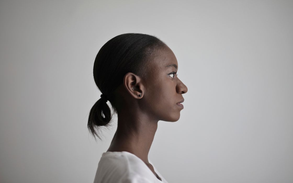 Side profile of a woman with her hair tied back, showing her ear, against a plain white background.
