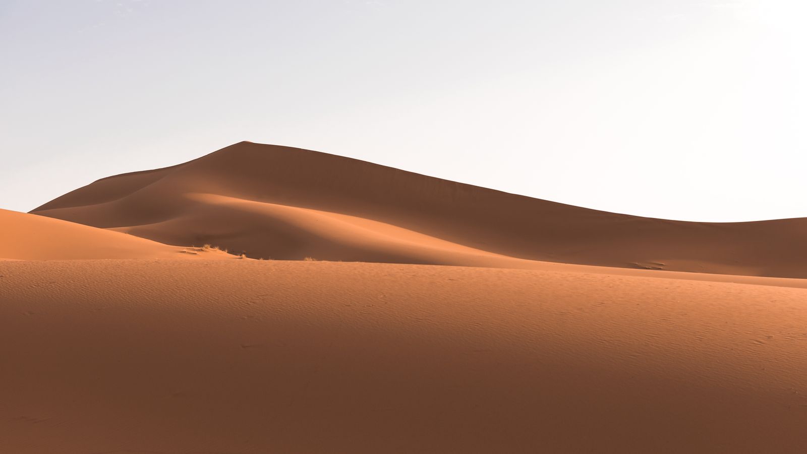 Rust-red desert dunes meeting a pale clay pan at sunrise