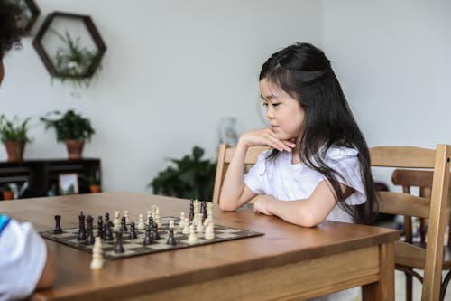 Free Asian girl playing chess with hand at chin Stock Photo