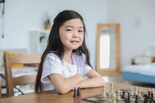 Free Cheerful Asian girl with long hair playing chess in bright cozy living room on blurred background Stock Photo