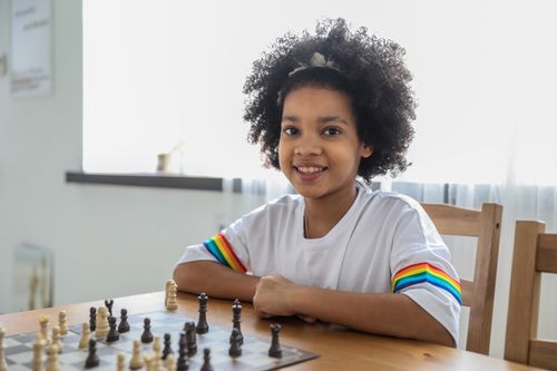 Free Smiling happy smart African American girl sitting at table with chessboard and learning chess game Stock Photo