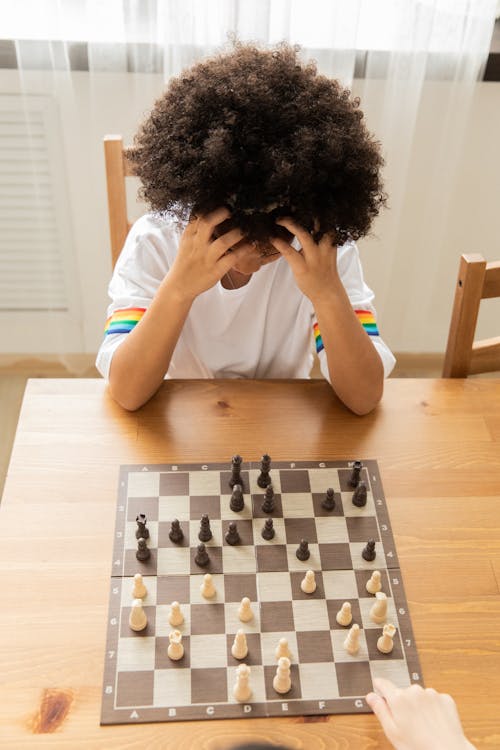 Free From above of clever African American girl playing chess game with crop anonymous opponent at table Stock Photo