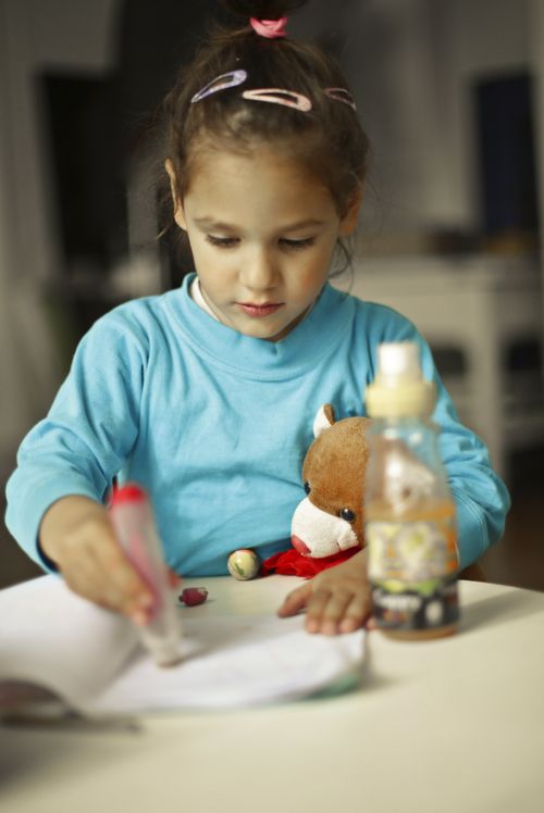 Free A young girl coloring with a teddy bear beside her, creating an innocent scene. Stock Photo