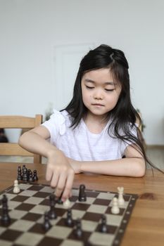 聪明可爱的亚洲女孩在木材桌上移动棋子，同时采用倾斜策略