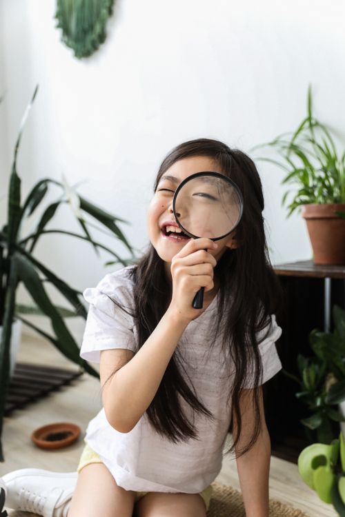 Free Smiling cheerful Asian girl with magnifier looking at camera in room with green potted plants Stock Photo