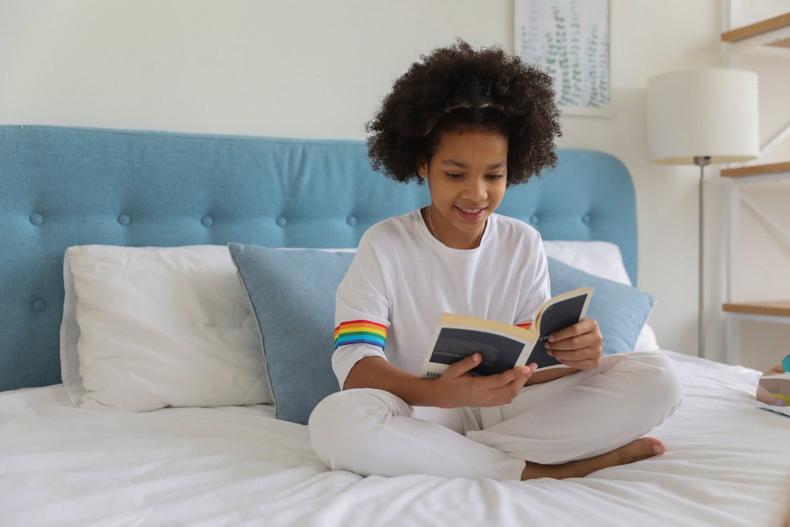 Free Black girl reading book on bed Stock Photo