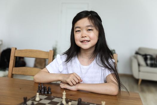 Happy cute Asian girl sitting at table with chessboard