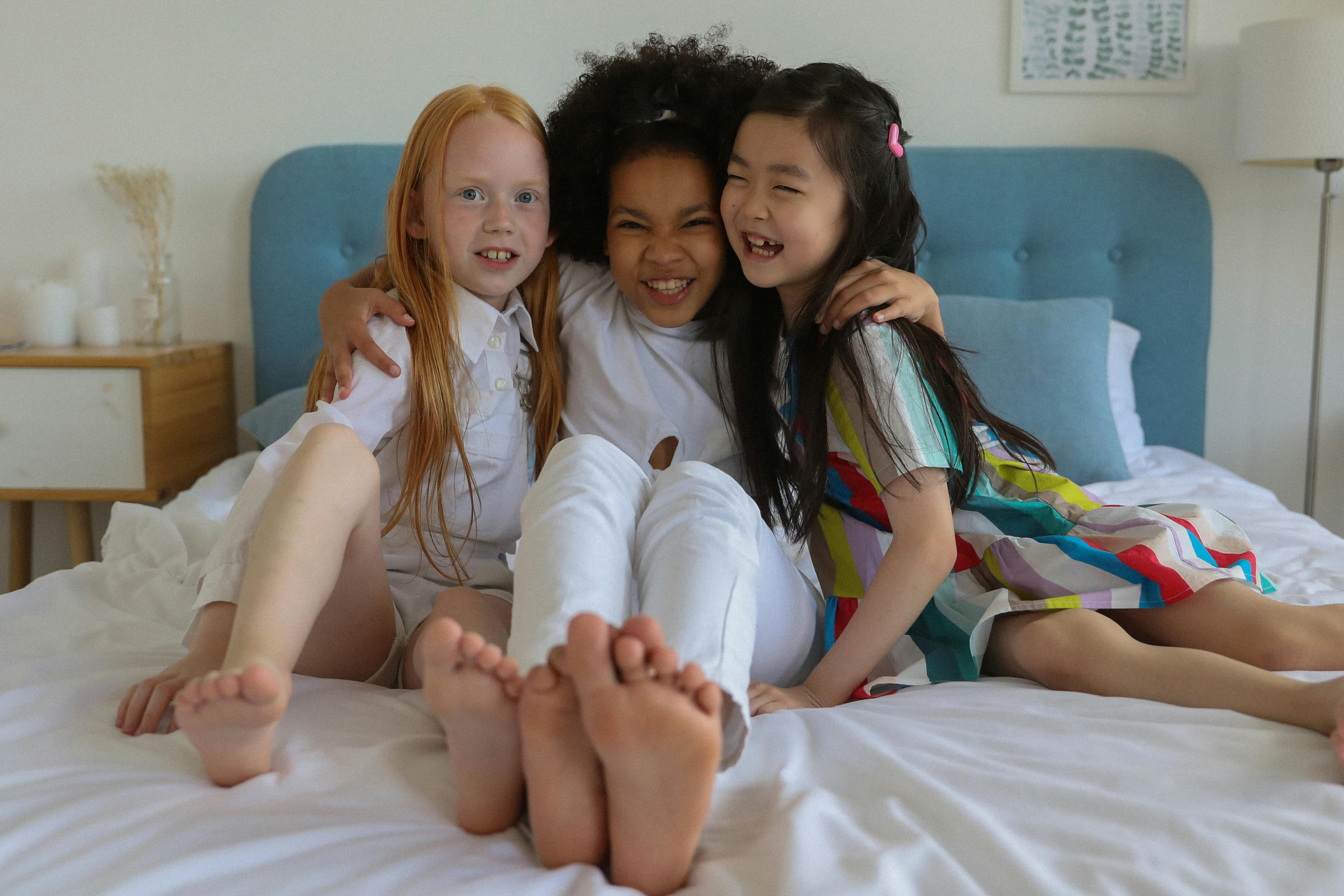 multiracial happy barefoot girls grimacing on bed