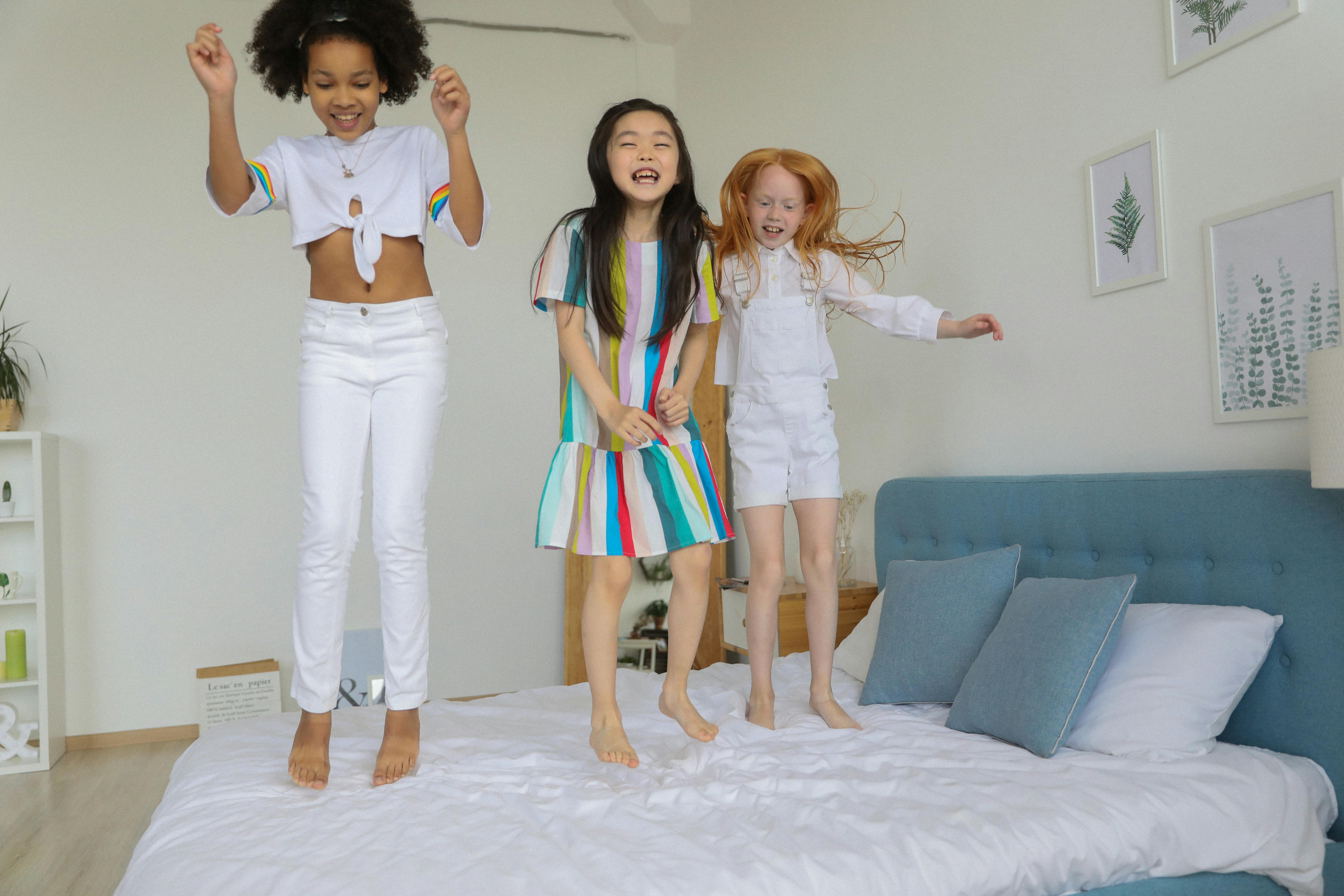 happy playful diverse girls jumping on bed