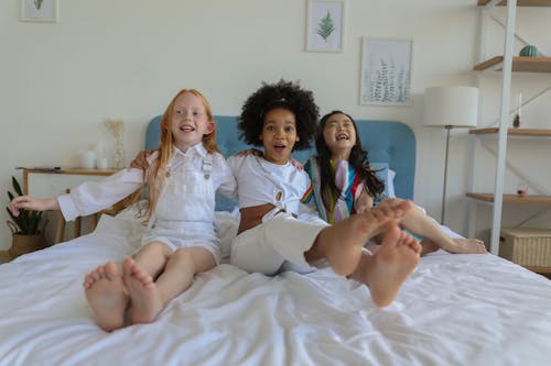 Free Cute funny cheerful multiracial girls resting and laughing on bed Stock Photo