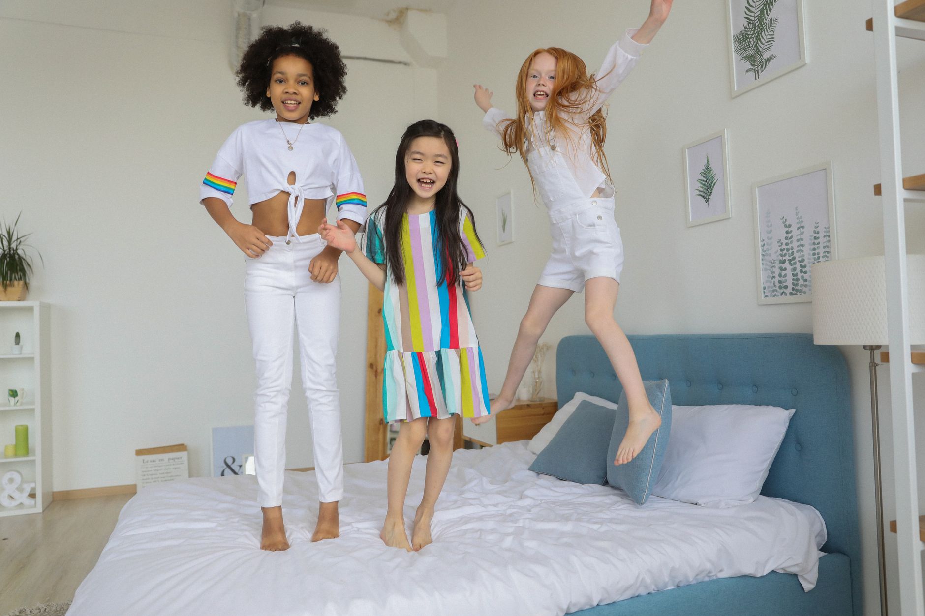 Cheerful happy diverse girls jumping and having fun on comfortable bed in modern room