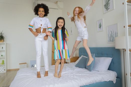 Multiracial smiling girls jumping on soft cozy bed