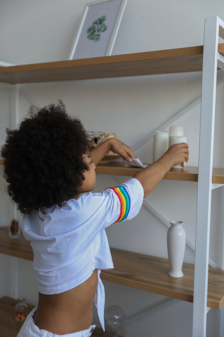 Ethnic Girl Cleaning Shelf At Home