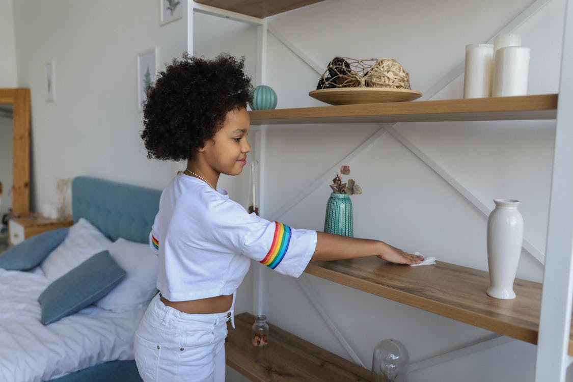 Small girl cleaning shelf in apartment