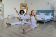 Full body multiracial girls performing splits happily sitting on floor in light bedroom