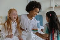 Group of multiracial girls spending time at home and laughing happily on bed