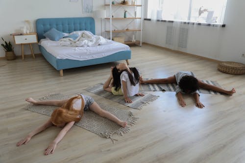 Free Group of multiethnic little girls stretching on rugs on floors spending time together Stock Photo