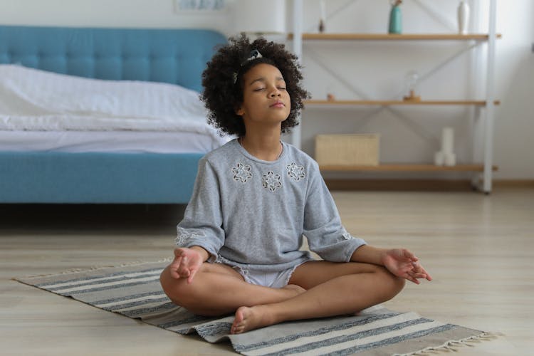 Black Child Meditating On Carpet In Room