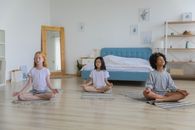 明亮的房间里，一位穿着休闲服的多民族女孩正闭眼冥想，双臂交叉放在腿上