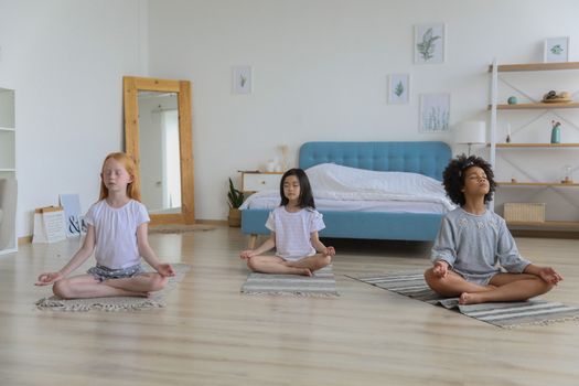 明亮的房间里，一位穿着休闲服的多民族女孩正闭眼冥想，双臂交叉放在腿上