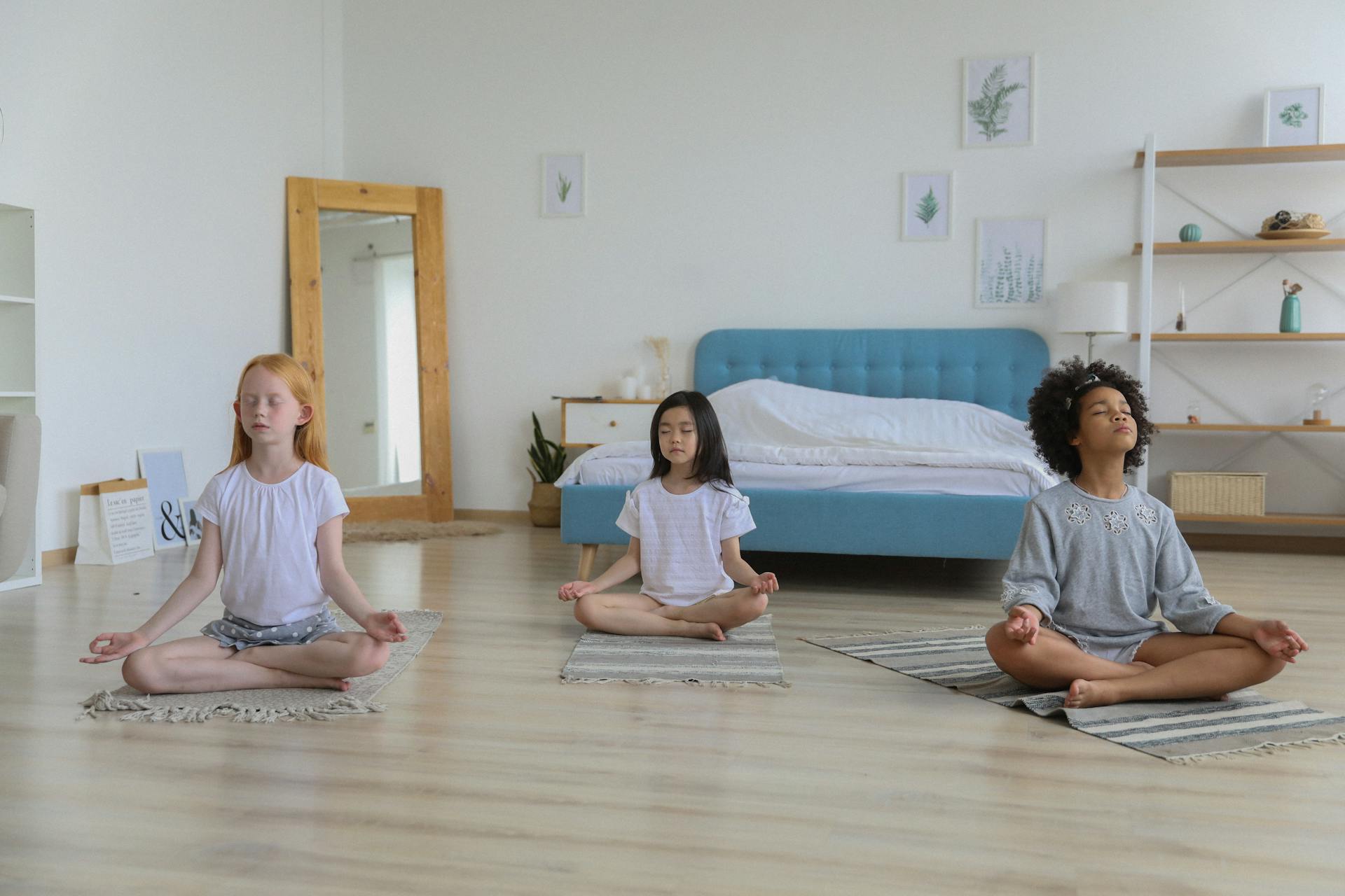 Full body of concentrated multiethnic girls in casual clothing meditating in bright room with eyes closed and arms folded on crossed legs