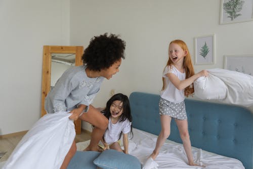 Cheerful girls fighting with pillows on bed