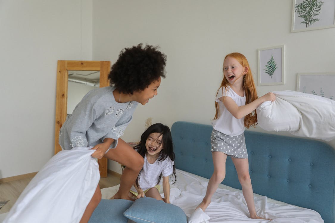 Free Cheerful girls fighting with pillows on bed Stock Photo
