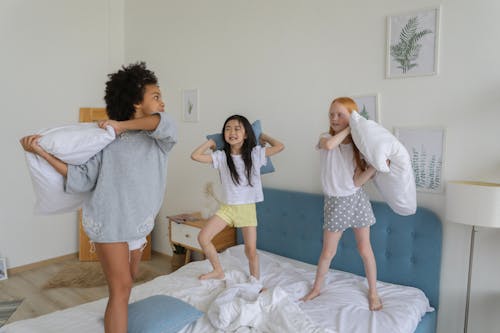 Full body of cheerful multiracial girls using pillows while playing in bright cozy room in daytime