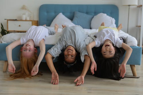 Cheerful multiracial children in casual clothes lying on comfortable bed while spending free time together