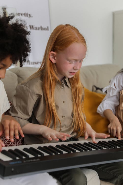 Веселая маленькая девочка играет на синтезаторе с друзьями