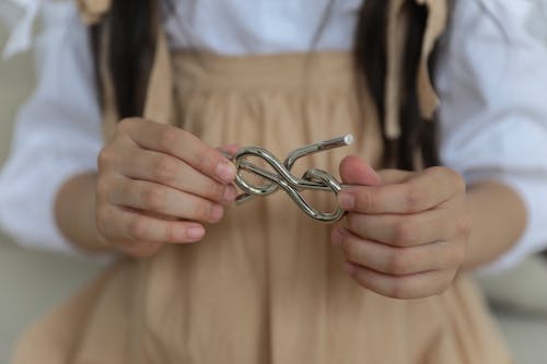 Crop anonymous child in casual wear holding metal wire brain teaser in shape of knot while playing at home